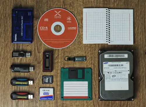 Tisch mit diversen Speichermedien, wie CD, Festplatte, Diskette, USB Sticks, Notizbuch