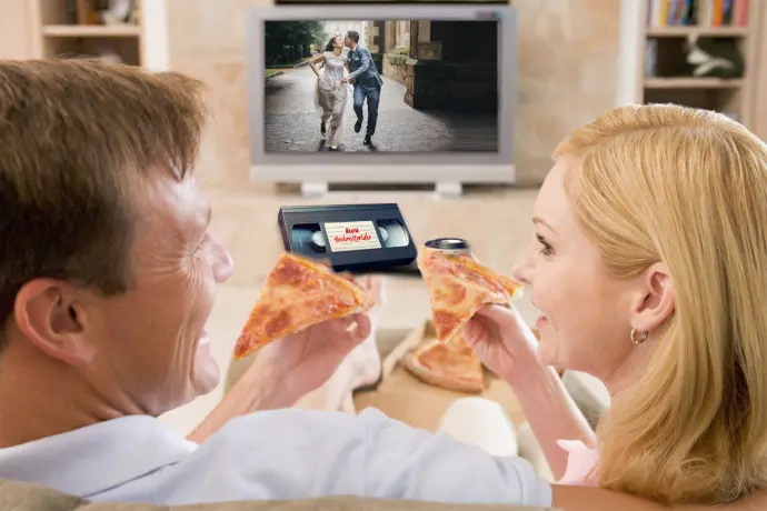 glückliches pärchen sitzt vor dem TV und sieht sich ihr digitalisiertes Hochzeitsvideo an.