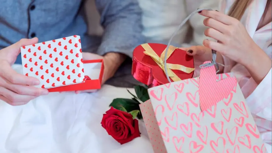 Aktion €99 - Geschenkidee für das persönlichste Geschenk - Wertvolle Erinnerungen digital erleben. Ein verliebtes Paar tauscht sich gegenseitig Geschenke aus, Verpackungen mit Herzen und Rose