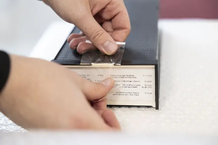 Hände kleben eine Beschriftung mit Inhaltsangaben auf eine VHS - Kassette – Vorbereitung für die digitale Archivierung bei FORVIDEO Dias_ versand